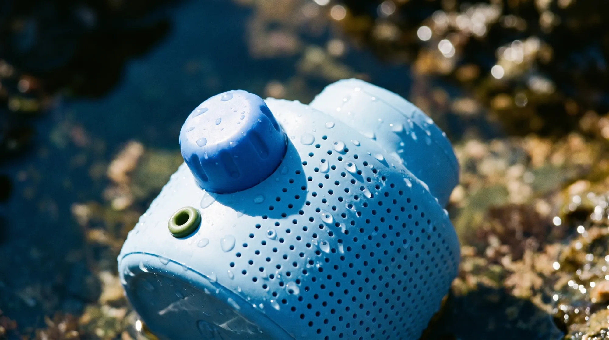 Close-up of a Murmur speaker in shallow pond water with droplets on its surface